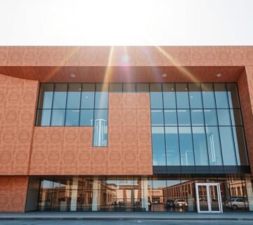 A sleek, modern sandwich panel building with clean lines and a glass front, situated in the bustling city of Dammam. The exterior features intricately textured insulated panels in a warm, earthy tone, seamlessly blending function and form. Sunlight streams through the large windows, creating a bright and inviting atmosphere. The structure stands as a testament to the innovative use of materials in contemporary construction, showcasing the versatility and durability of sandwich panels in the creation of efficient, visually striking architectural spaces.